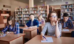 Uczniowie w bibliotece piszą test. Zastanawiają się, ile trwa szkoła zaoczna, gdy skupiają się na zadaniach.