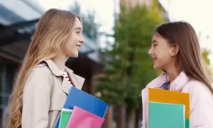 Dwie uczennice rozmawiają, trzymając zeszyty. Być może omawiają rekrutację uzupełniającą do szkół średnich.