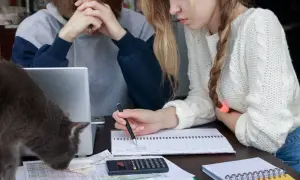 Dwie osoby przy biurku, jedna zrezygnowana, druga próbuje pomóc. Jak rozmawiać z nastolatkiem który nie chce się uczyć, gdy kot przeszkadza?