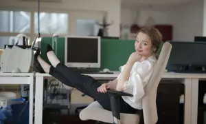 Technik administracji w biurze, z nogami na biurku, odpoczywa po wykonaniu zadań.