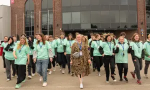 Grupa młodych ludzi w zielonych koszulkach idzie przed budynkiem. Pewnie zastanawiają się, ile lat w liceum spędzą na nauce i zabawie.