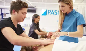 Młodzi ludzie uczą się masażu, zdobywając zawody medyczne bez studiów. Instruktor pokazuje techniki.