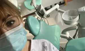 Praktyki asystentka stomatologiczna w gabinecie. Widoczny fragment twarzy w maseczce, okulary i fartuch z motywem zębów.