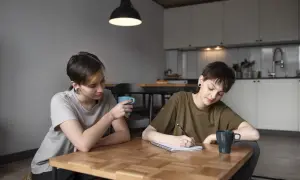 Dwie osoby przy stole, jedna pisze, druga pije kawę. Rozmowa o tym, jak załatwić zaświadczenie o dysleksji, może być wsparciem w nauce.