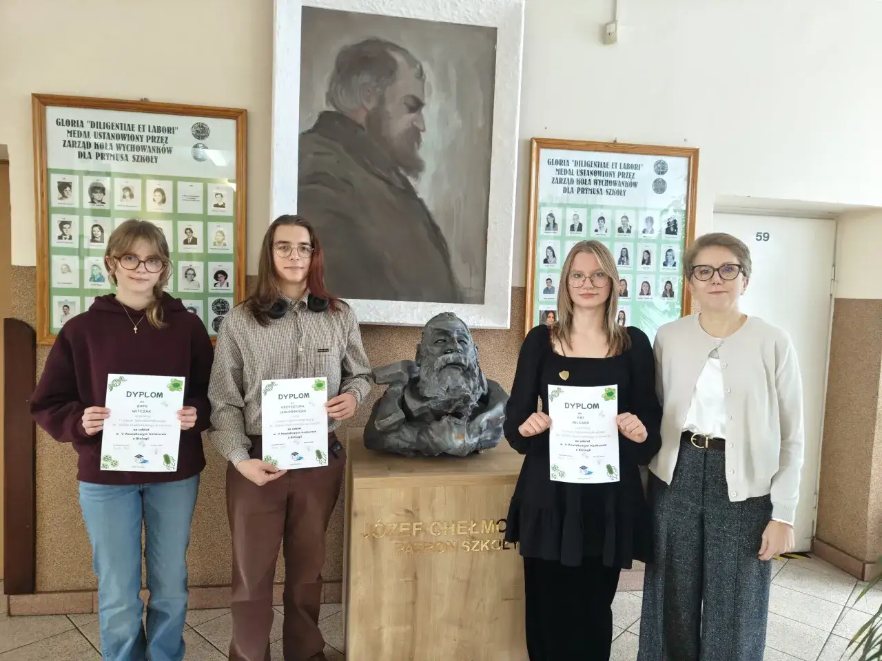 Uczniowie z dyplomami przed portretem patrona szkoły. Stypendium w liceum jest przyznawane za wybitne osiągnięcia.