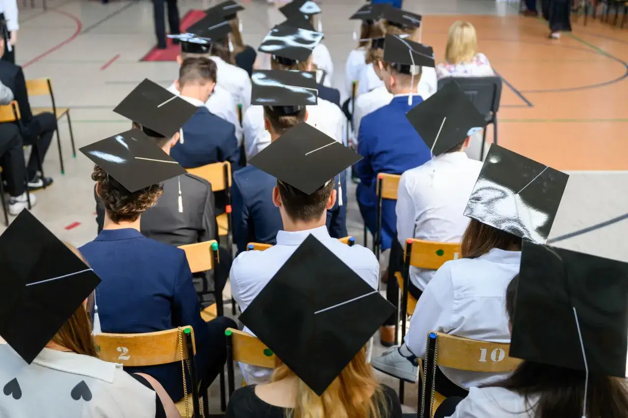 Uczniowie w biretach czekają na zakończenie uroczystości. To ważny moment, być może związany z rekrutacją uzupełniającą do szkół średnich.