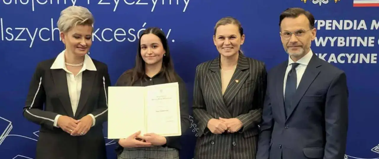 Uczennica odbiera dyplom. W tle napis 