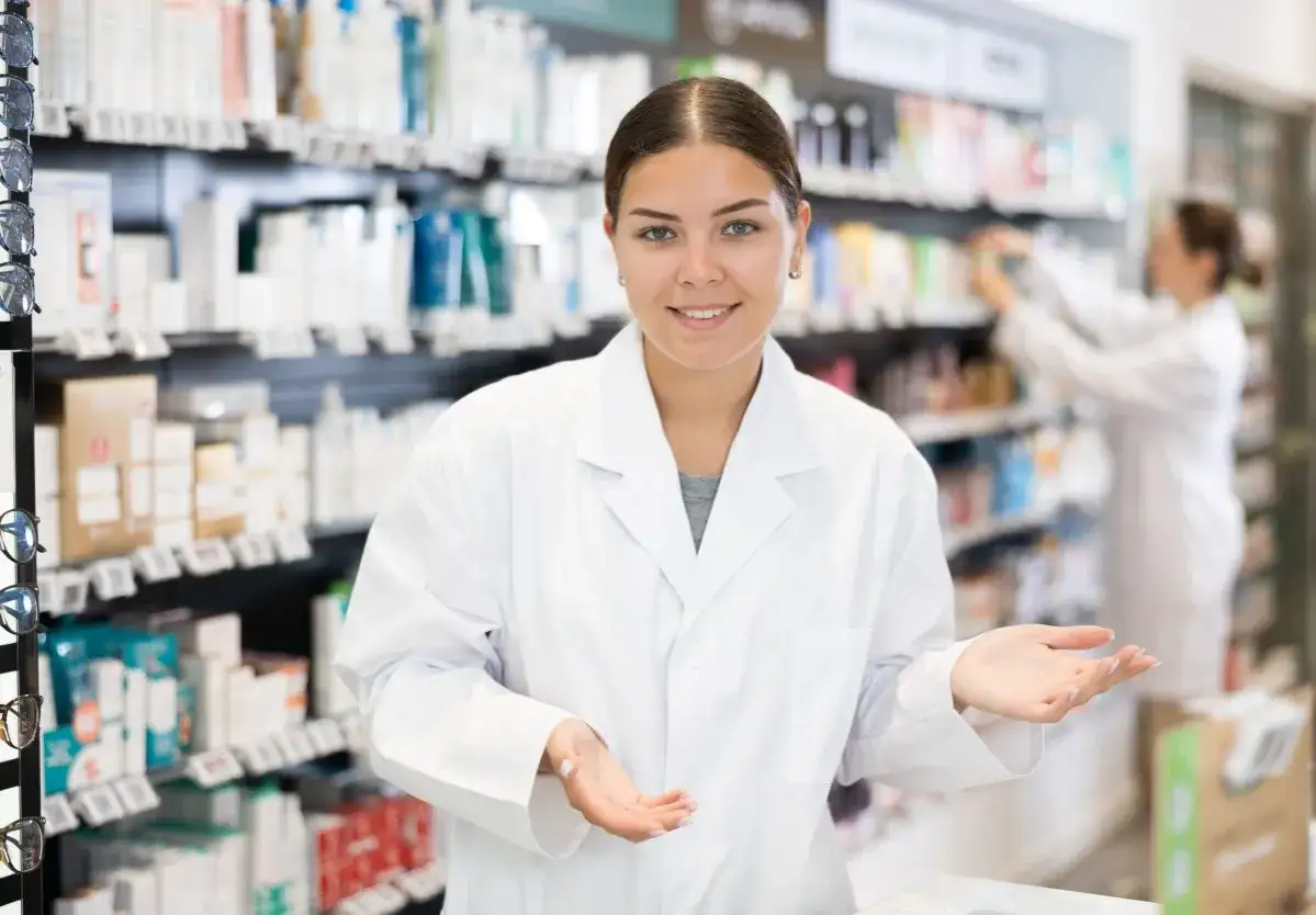 Farmaceutka w białym fartuchu, uśmiechnięta, pokazuje, co daje wpis do rejestru zawodów medycznych – dostęp do wiedzy i profesjonalnej obsługi.