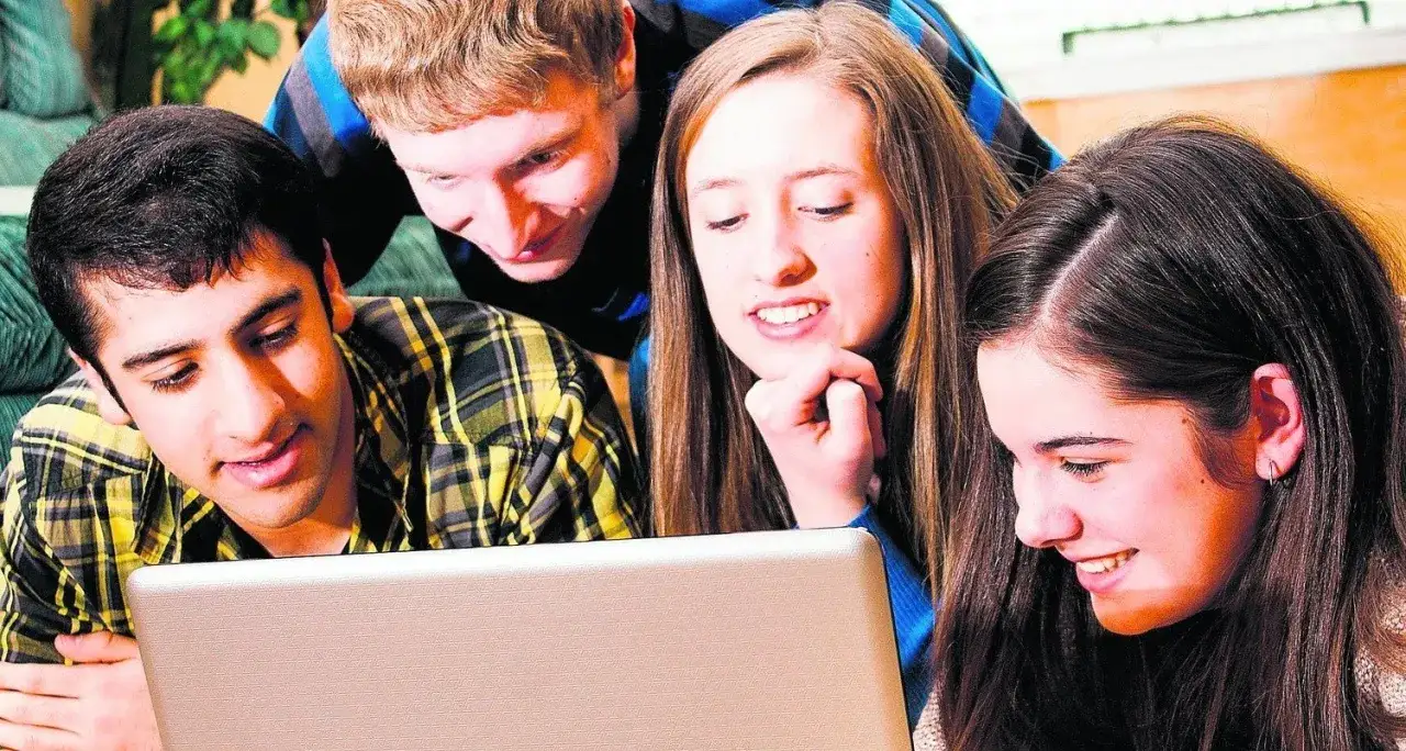 Grupa nastolatków wspólnie szuka informacji, jak wybrać szkołę średnią, przeglądając coś na laptopie.