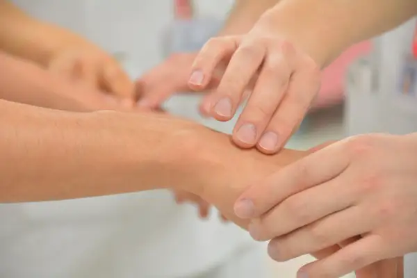 Terapia zajęciowa: dłonie terapeuty badają nadgarstek pacjenta. To pierwszy krok, by dowiedzieć się, jak zostać terapeutą zajęciowym.